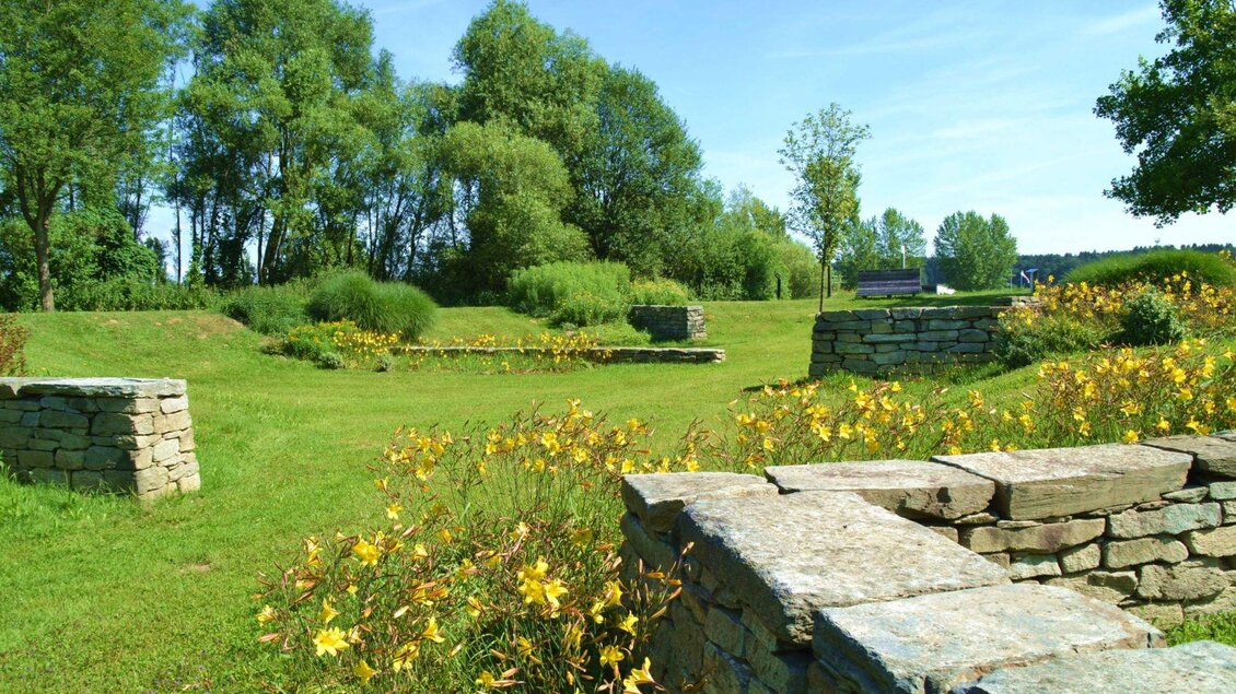 Eine grüne Wiese mit bunten Blumen und verstreuten Steinmauern. Im Hintergrund sind hohe Bäume und ein blauer Himmel zu sehen. | © Kurkommission Bad Blumau
