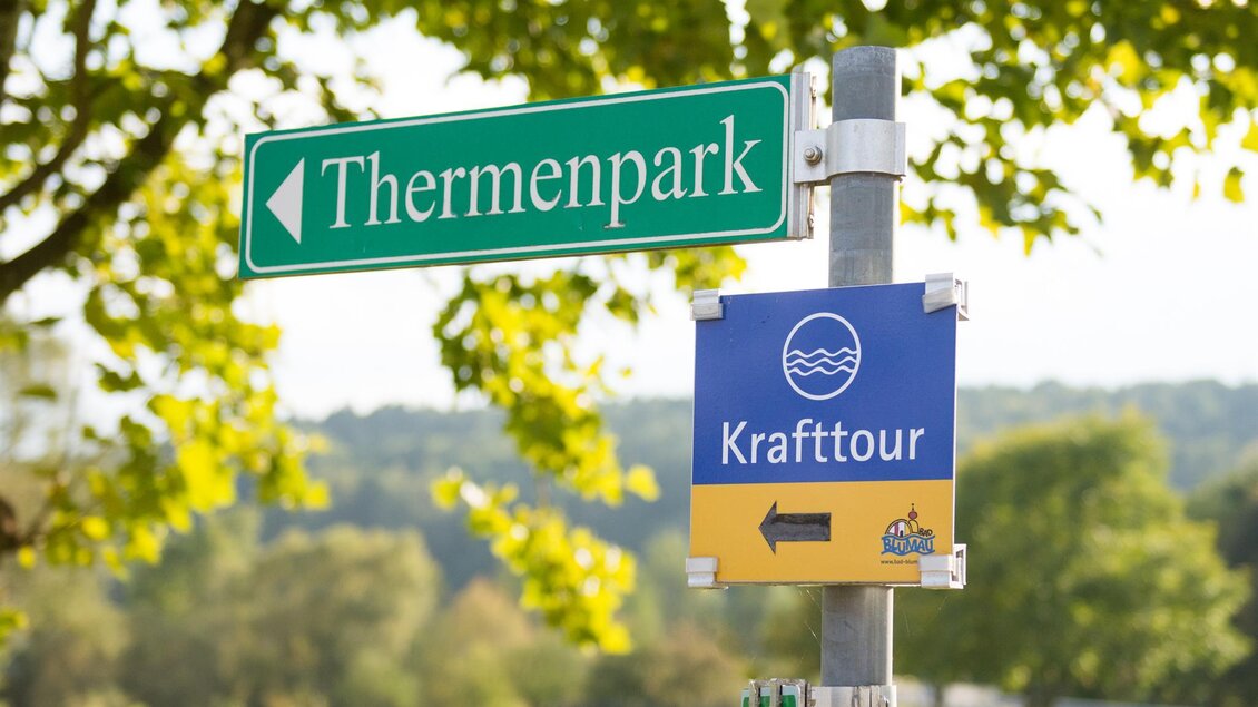 Ein Wegweiser zeigt Richtung Thermenpark und zur Krafttour. Die Umgebung ist grün mit Bäumen. | © Kurkommission Bad Blumau