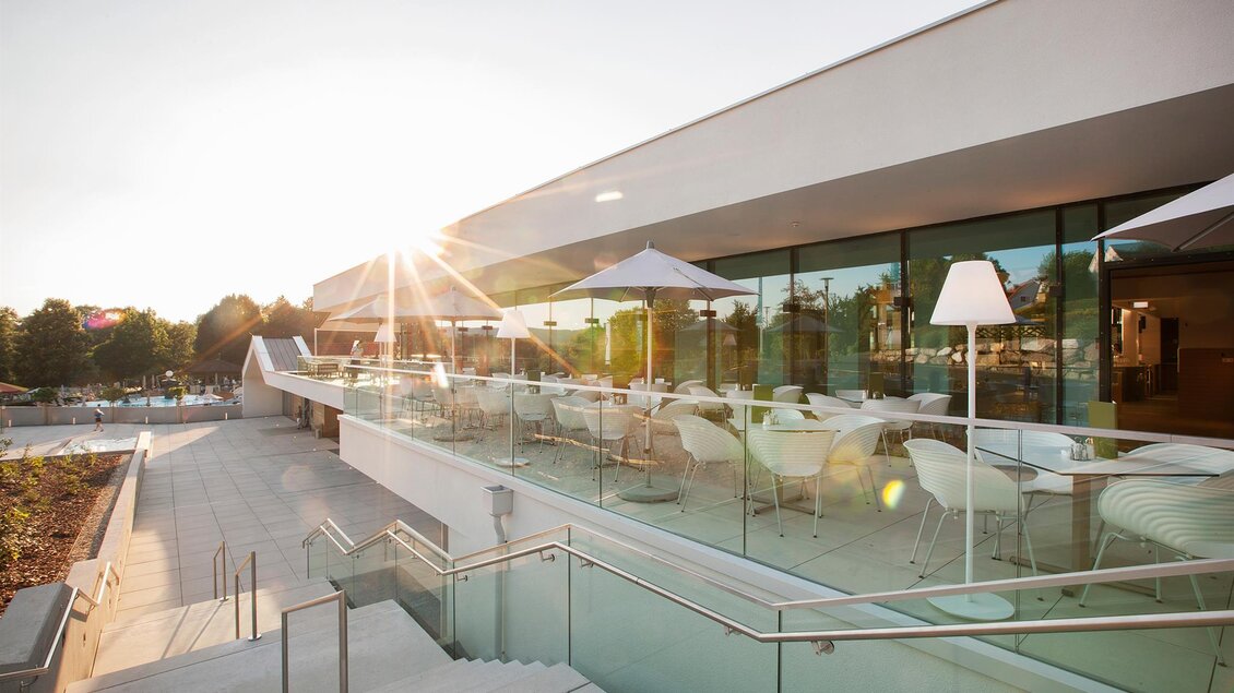 Eine moderne Terrasse mit Glasgeländer und weißen Möbeln. Die Sonne scheint und verleiht der Umgebung eine gemütliche Atmosphäre. | © Eisenberger