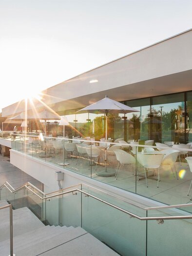 A modern terrace with glass railing and white furniture. The sun is shining, giving the surroundings a cozy atmosphere. | © Eisenberger