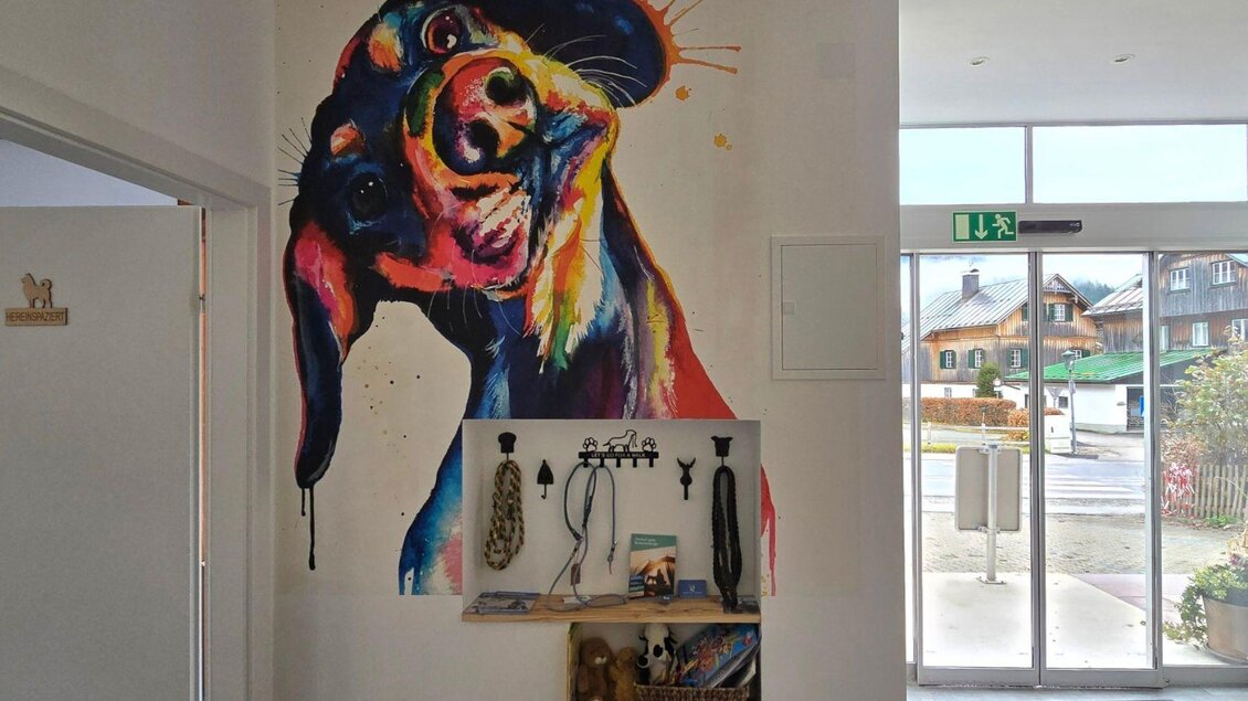 Ein farbenfrohes Wandgemälde eines Hundes schmückt den Raum. Unter dem Bild befinden sich Haken für Hundezubehör. | © Stephanie Bor