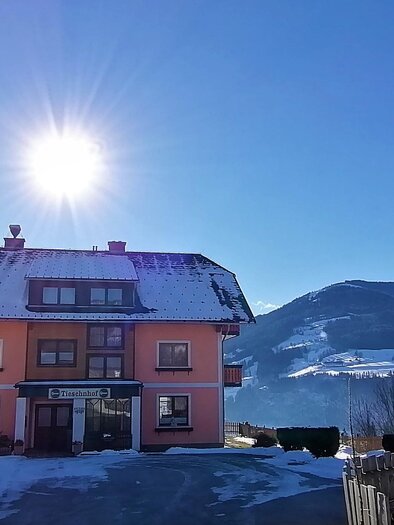 Ein schön gelegenes Haus im Schnee, umgeben von Bergen. Die Sonne scheint strahlend am blauen Himmel. | © Tieschnhof