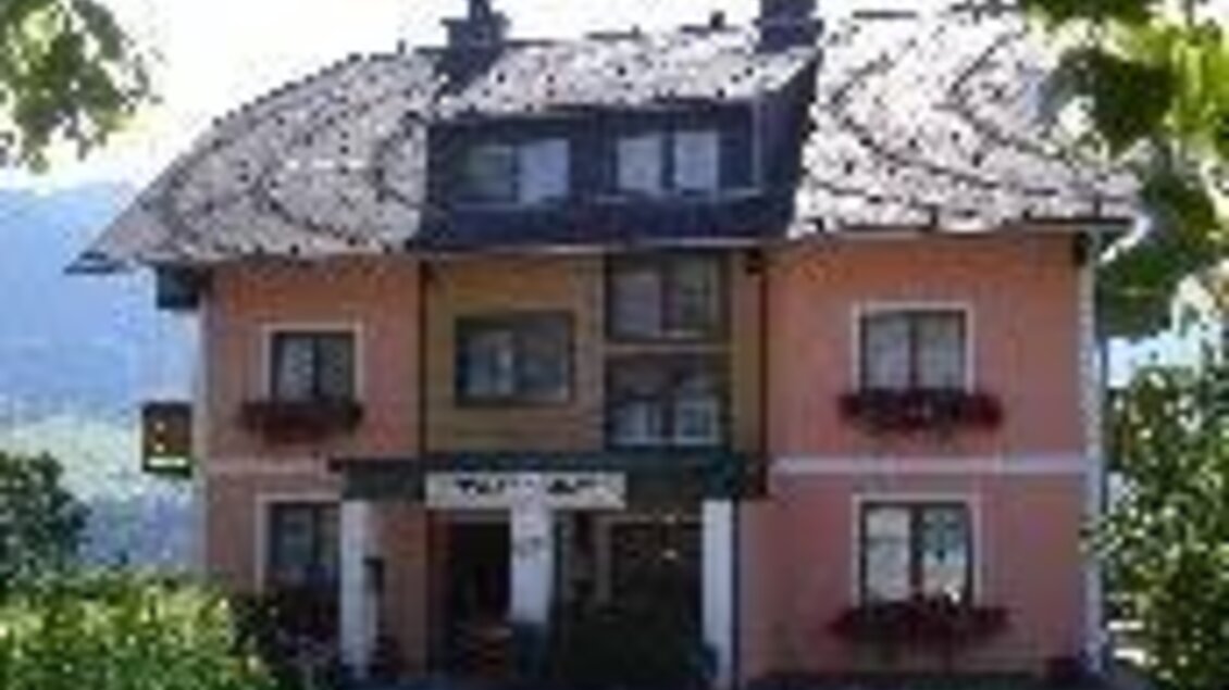 Ein charmantes Haus mit rosa Fassaden und einem grünem Balkon. Umgeben von grünen Bäumen und den Bergen im Hintergrund. | © Tieschnhof