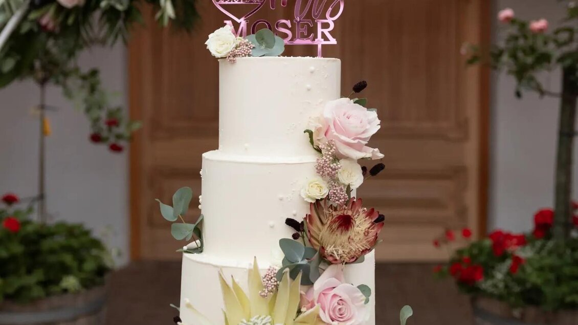 Eine elegante Hochzeits-Torte mit mehreren Etagen, dekoriert mit frischen Blumen. Oben steht ein „Mr & Mrs“ Schriftzug in Rosa. | © Martina Pöltl / Nilepixx by Nicky Hoferfotografie