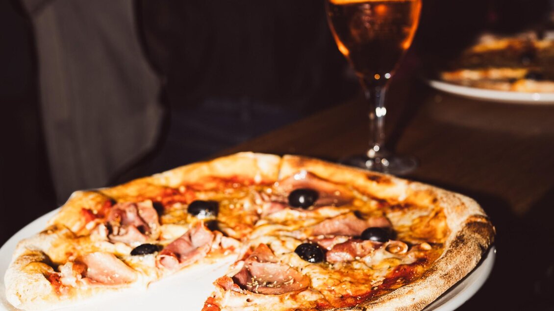 Frisch gebackene Pizza mit Schinken und Oliven neben einem Glas Aperitif im Tintenfass Graz | © Chiara Maria B.