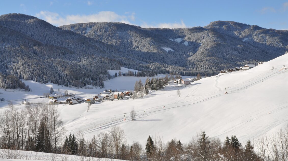 Eine winterliche Landschaft mit schneebedeckten Hügeln und schönen Bergen im Hintergrund. Kleine Häuser liegen malerisch in der verschneiten Ebene. | © Tourismusverband Murau