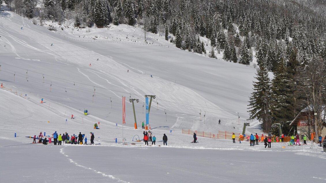 Eine verschneite Winterlandschaft mit vielen Menschen, die Skifahren. Im Hintergrund sind Bäume und schneebedeckte Pisten zu sehen. | © Tourismusverband Murau