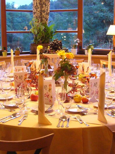 Ein elegant gedeckter Tisch mit einer runden Tischdecke in Gelb. Er ist mit Besteck, Gläsern und dekorativen Elementen geschmückt, umrahmt von großen Fenstern mit Blick auf die Natur. | © Legenstein