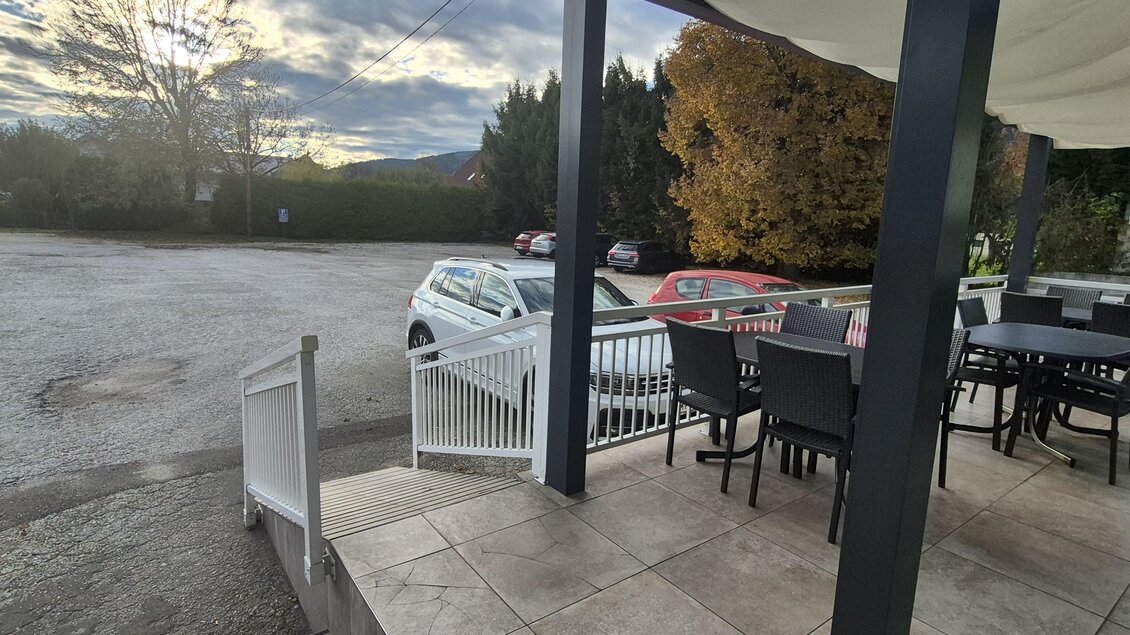 Eine Terrasse mit Tischen und Stühlen blickt auf einen leeren Parkplatz. Der Himmel ist bewölkt und die Bäume sind bunt. | © TV Hochsteiermark