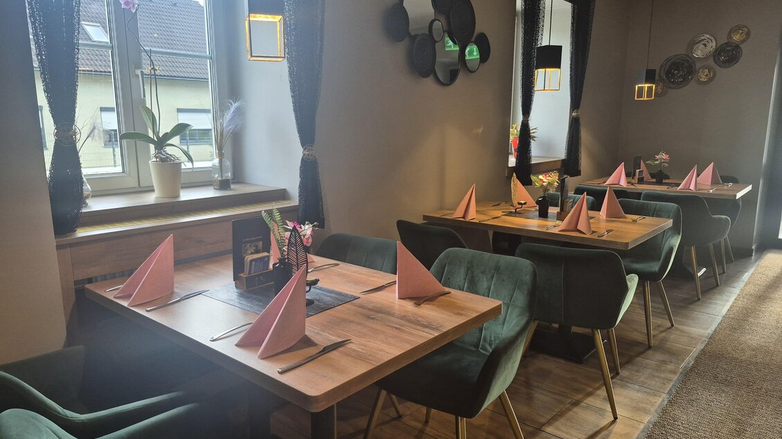 Ein gemütliches Restaurant mit Holztischen und bequemen grünen Stühlen. Die Tische sind mit roten Servietten dekoriert und es gibt große Fenster mit natürlichem Licht. | © TV Hochsteiermark