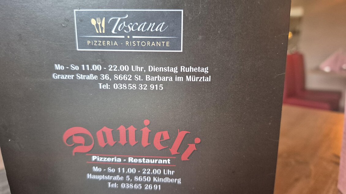 Das Bild zeigt eine Restaurant- und Pizzakarte. Die Informationen zu den Öffnungszeiten und Standorten von Toscana und Danieli sind deutlich sichtbar. | © TV Hochsteiermark