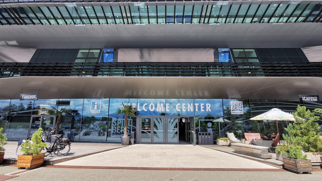 Ein modernes Gebäude mit der Aufschrift "WELCOME CENTER". Vor dem Eingang stehen Pflanzen und ein Tisch mit Sonnenschirm. | © Patrizia Schreibmayr