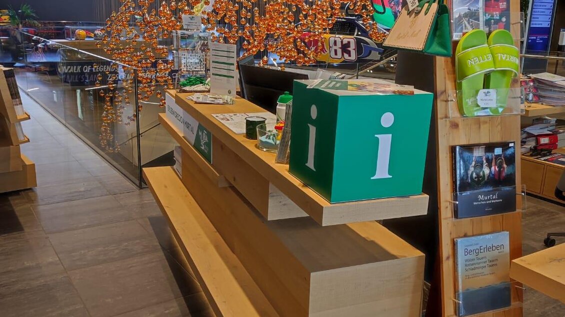 Ein moderner Empfangsbereich mit einem Informationsstand in grüner Farbe. Im Hintergrund ist eine kreative Installation aus bunten Elementen zu sehen. | © Patrizia Schreibmayr