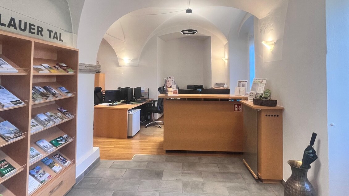 Ein Empfangsbereich mit einem Holzschalter und mehreren Computerarbeitsplätzen. Auf der linken Seite befinden sich Informationsbroschüren in einem Regalsystem. | © Tourismusverband Oststeiermark