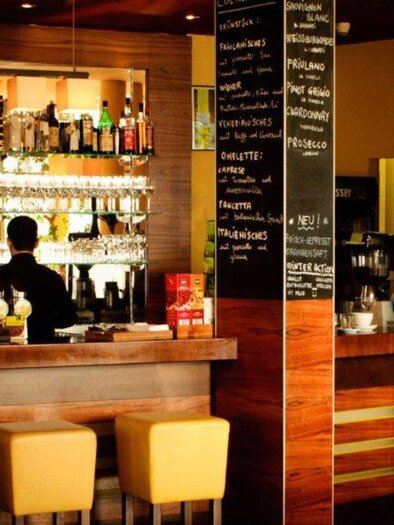 Eine stilvolle Bar mit einem Holztresen und Regalen voller Getränke. Im Hintergrund sind Tische und Stühle zu sehen, die eine gemütliche Atmosphäre schaffen. | © Trattoria Siena