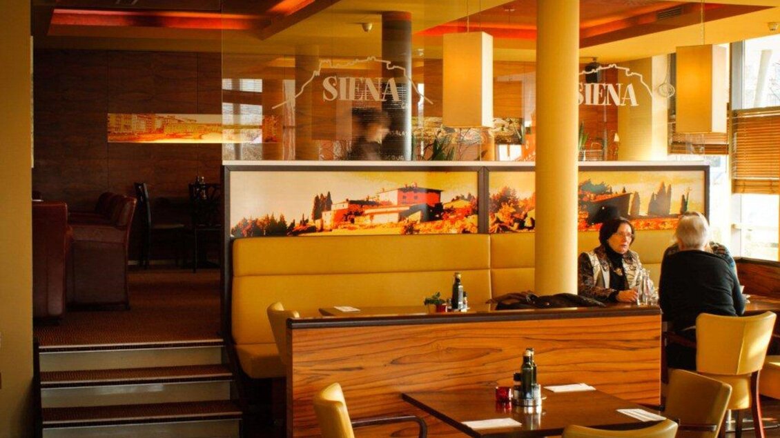 Ein gemütliches Restaurant mit stilvollen Sitzbereichen und warmem Licht. Zwei Gäste unterhalten sich an einem Tisch. | © Trattoria Siena