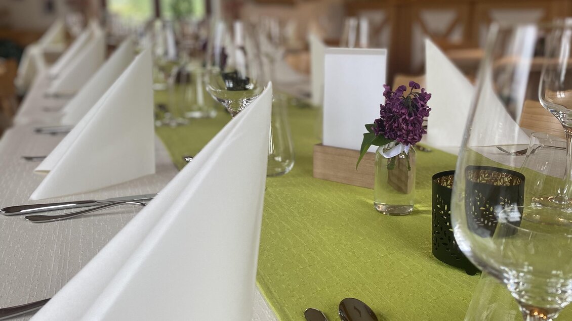 Ein elegant gedeckter Tisch mit weißen Servietten und Gläsern. Die Tischdecke ist grün, und es gibt kleine Blumenarrangements.