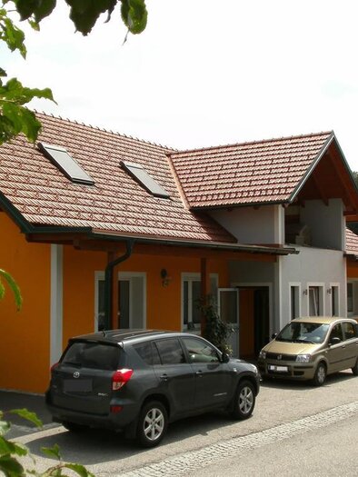 Ein modernes Gebäude mit orangefarbener Fassade und rotem Dach. Mehrere Autos parken vor dem Haus. | © Franz Zweiger