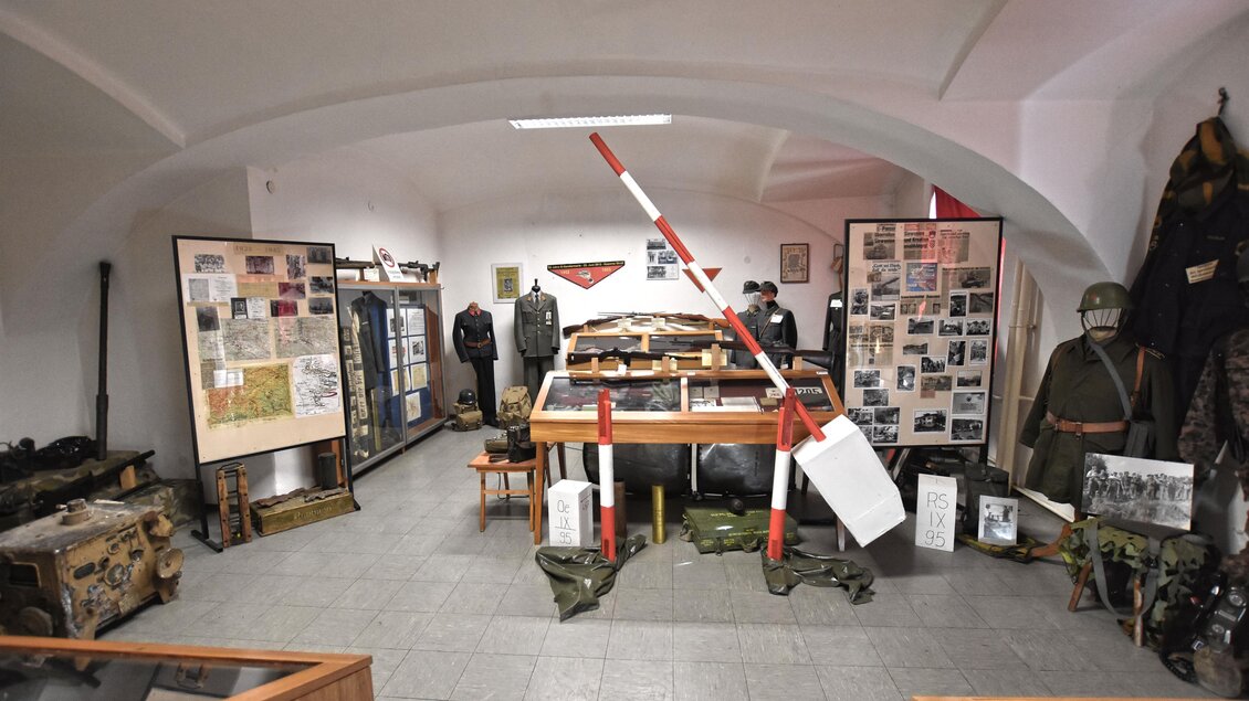 Ein historisches Museum mit verschiedenen Exponaten, darunter Uniformen und Fotos. In der Mitte ist ein Tisch mit weiteren Ausstellungsstücken. | © BMLV/Robert Gießauf
