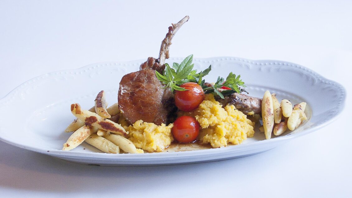 Ein ansprechender Teller mit Lammkotelett, cremigem Kartoffelbrei und Kirschtomaten. Dazu gibt es knusprige Pommes frites und frische Kräuter. | © Tscheppe