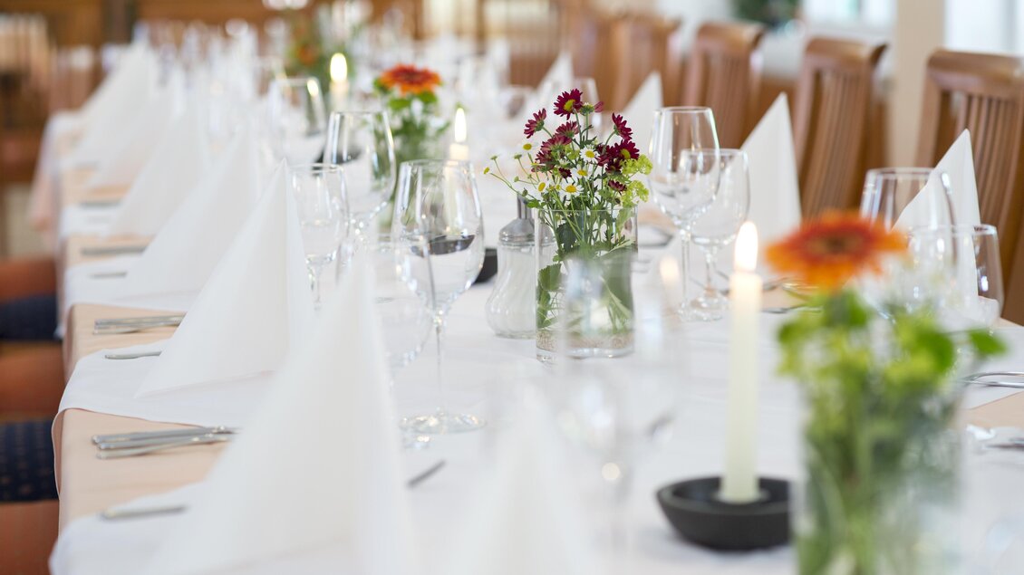 Ein elegant gedeckter Tisch mit weißen Servietten und Gläsern. Kleine Blumenarrangements und Kerzen verleihen eine festliche Atmosphäre. | © Tscheppe