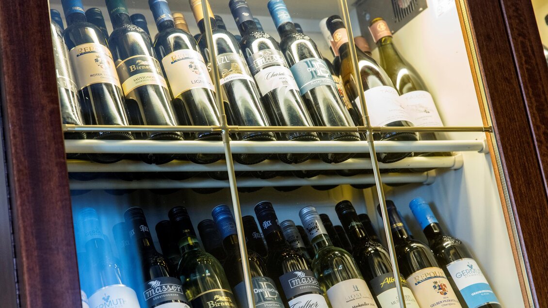 Eine Weinflaschenauswahl in einer Glasvitrine. Es sind verschiedene Weinsorten und -marken sichtbar. | © Tscheppe