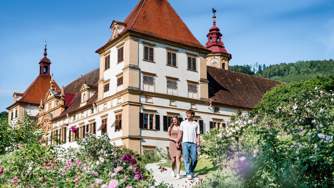 Ein Pärchen geht am geschotterten Weg in den Schlosspark, dahinter ist Schloss Eggenberg in Graz zu sehen.  | © Graz Tourismus-Mias Photoart