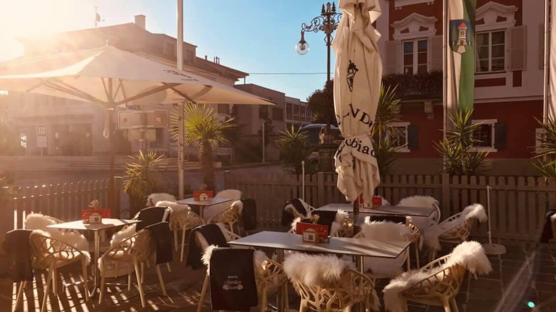 Ein gemütlicher Außenbereich mit weißen Stühlen und Tischen, dekoriert mit Fellauflagen. Die Sonne scheint hell auf die Szene, die von Pflanzen umgeben ist. | © Uptown Bistro