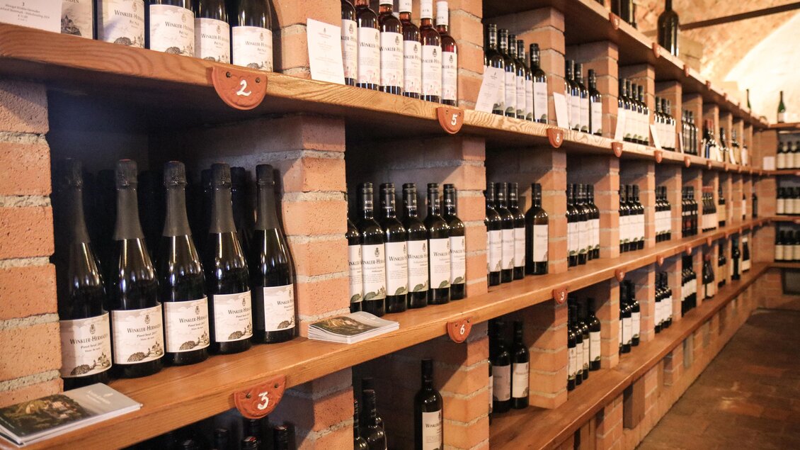 Ein Regal voller Weinflaschen in einem Weinlager. Die Flaschen sind ordentlich aufgereiht und bieten eine Vielzahl von Weinsorten. | © Winkler-Hermaden