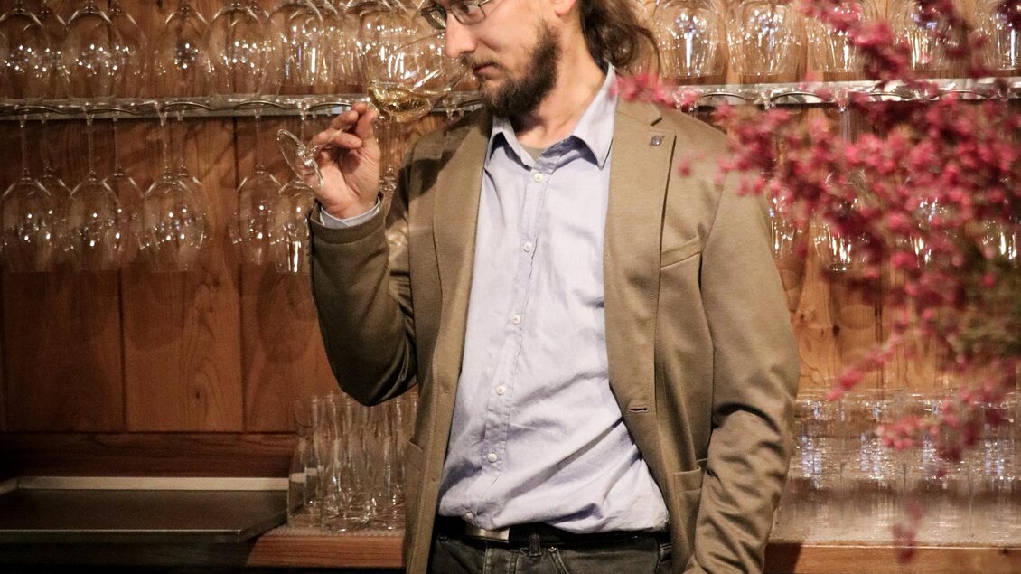 Ein Mann steht an einer Bar, umgeben von Glaswaren. Im Hintergrund sind Ziegelwände und eine dekorative Pflanze zu sehen. | © Winkler Hermaden