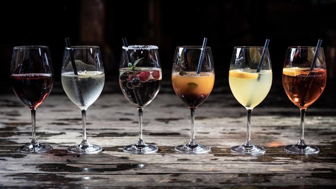 Sechs verschiedene Cocktails in Gläsern mit Strohhalmen auf einem Holzuntergrund. Die Getränke sind bunt und ansprechend angerichtet. | © © Urbanistub'n