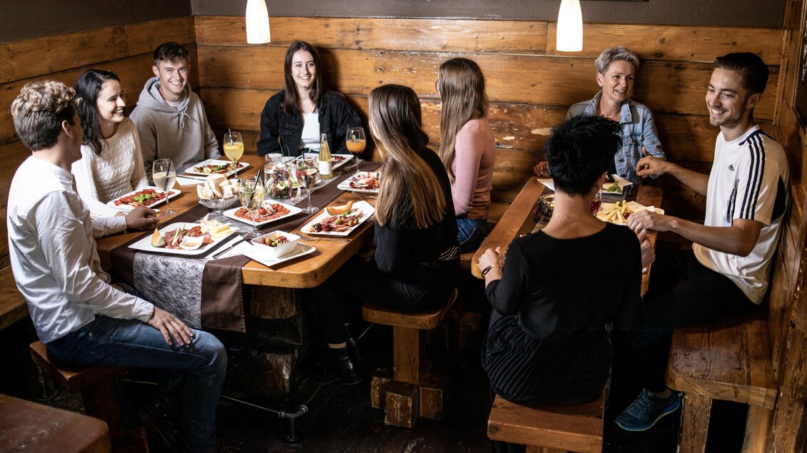 Eine Gruppe von Menschen sitzt an einem Holztisch und genießt eine Mahlzeit. Die Atmosphäre ist gemütlich und gesellig. | © © Urbanistub'n