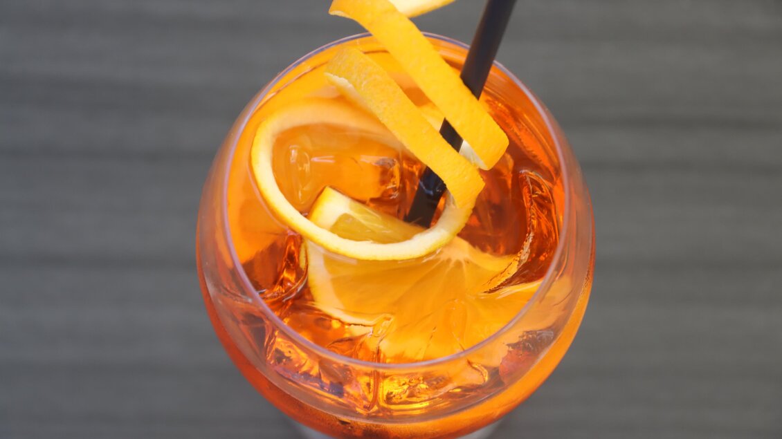 Ein erfrischendes Getränk in einem Glas mit Eiswürfeln und einem Strohhalm. Der Drink ist orangefarben und mit Zitronenscheiben dekoriert. | © © Urbanistub'n