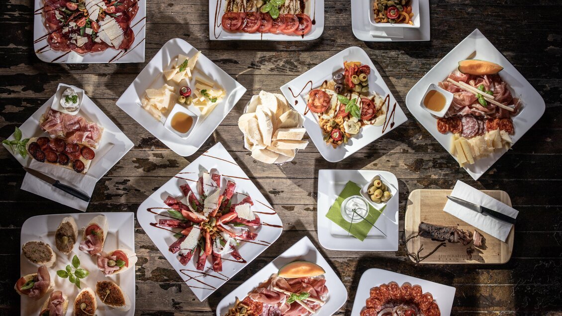 Ein stilvolles Arrangement von verschiedenen köstlichen Vorspeisen auf weißen Tellern. Die Platte umfasst Fleisch, Käse und frisches Gemüse. | © © Urbanistub'n