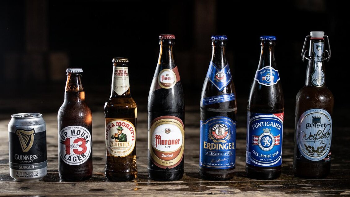 Eine Auswahl verschiedener Bierflaschen und -dosen, die auf einer Holzoberfläche stehen. Die Getränke zeigen unterschiedliche Marken und Stile. | © © Urbanistub'n