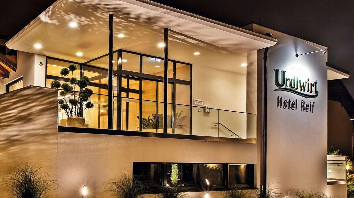 Ein modernes Hotelgebäude mit großflächigen Fenstern und einer eleganten Fassade. Der Eingang ist gut beleuchtet und einladend. | © Urdlwirt Hotel - Restaurant