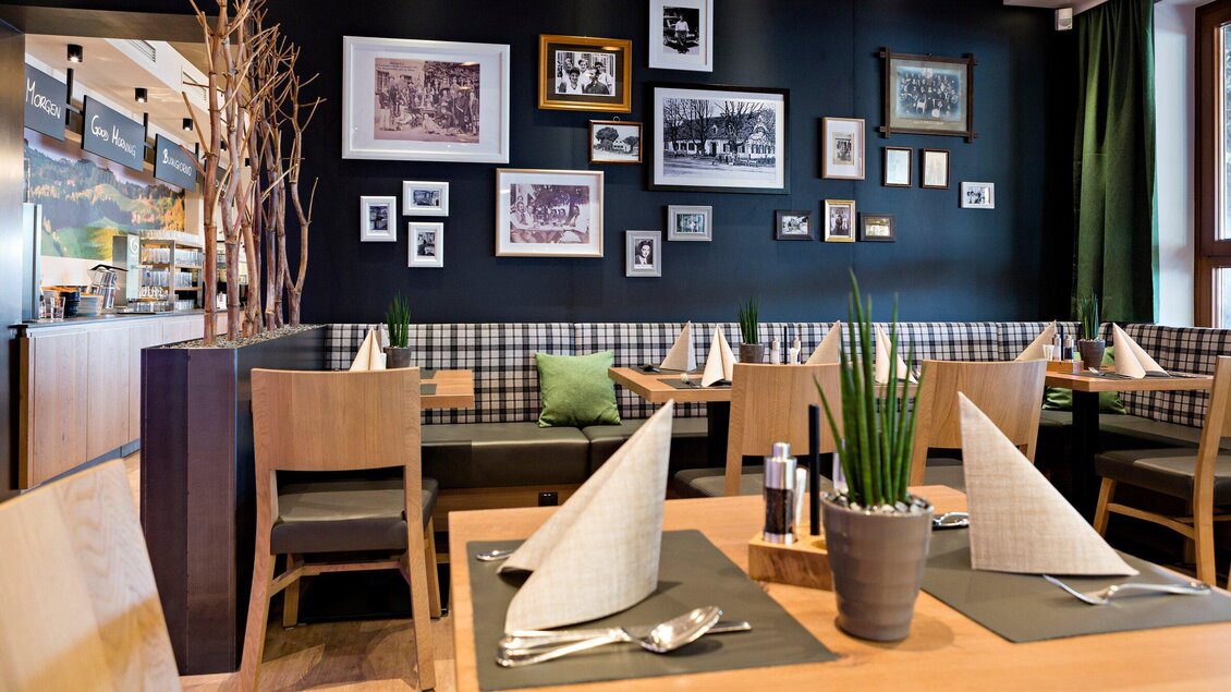 Ein gemütliches Restaurant mit stilvollen Holztischen und modernen Stühlen. An den Wänden hängen Bilder und Schwarz-Weiß-Fotografien, die eine einladende Atmosphäre schaffen. | © Urdlwirt Hotel - Restaurant
