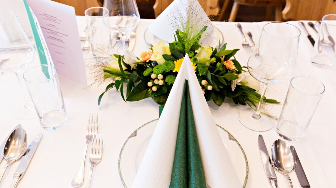 Ein schön gedeckter Tisch mit eleganten Bestecken und Gläsern. In der Mitte steht ein florales Arrangement mit Tischdekoration. | © Urdlwirt Hotel - Restaurant