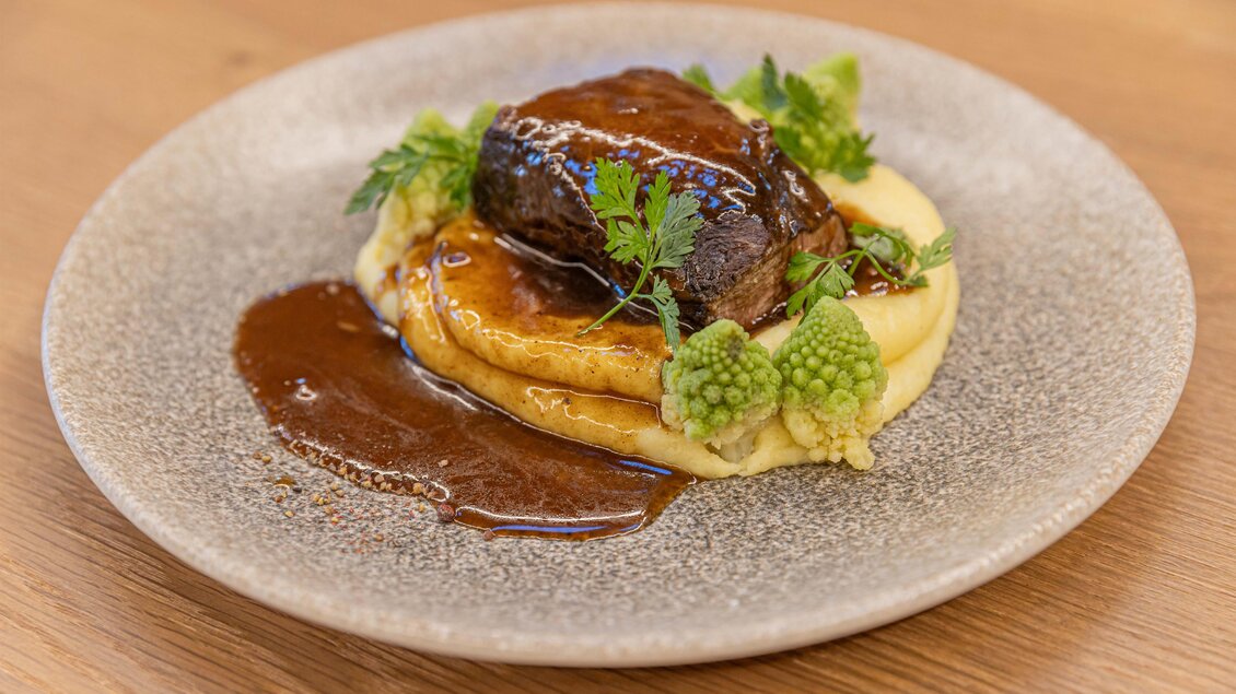 Ein zartes Stück Fleisch auf einem Bett aus cremigem Püree, garniert mit frischen Kräutern und buntem Gemüse. Serviert auf einem dekorativen Teller mit einer würzigen Soße. | © Urdlwirt Hotel -  Restaurant