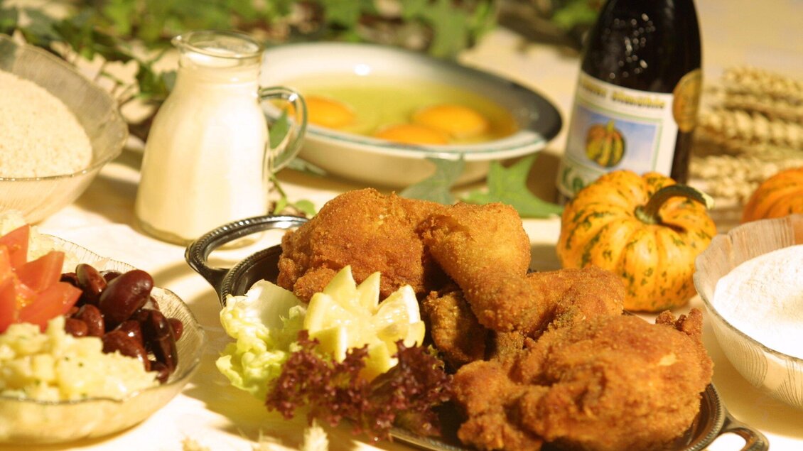 Ein appetitliches Gericht mit frittierter Hähnchenbrust auf einem silbernen Teller. Dazu sind frische Beilagen wie Salat, Gemüse und einige Zutaten für das Kochen zu sehen. | © Urdlwirt Hotel - Restaurant