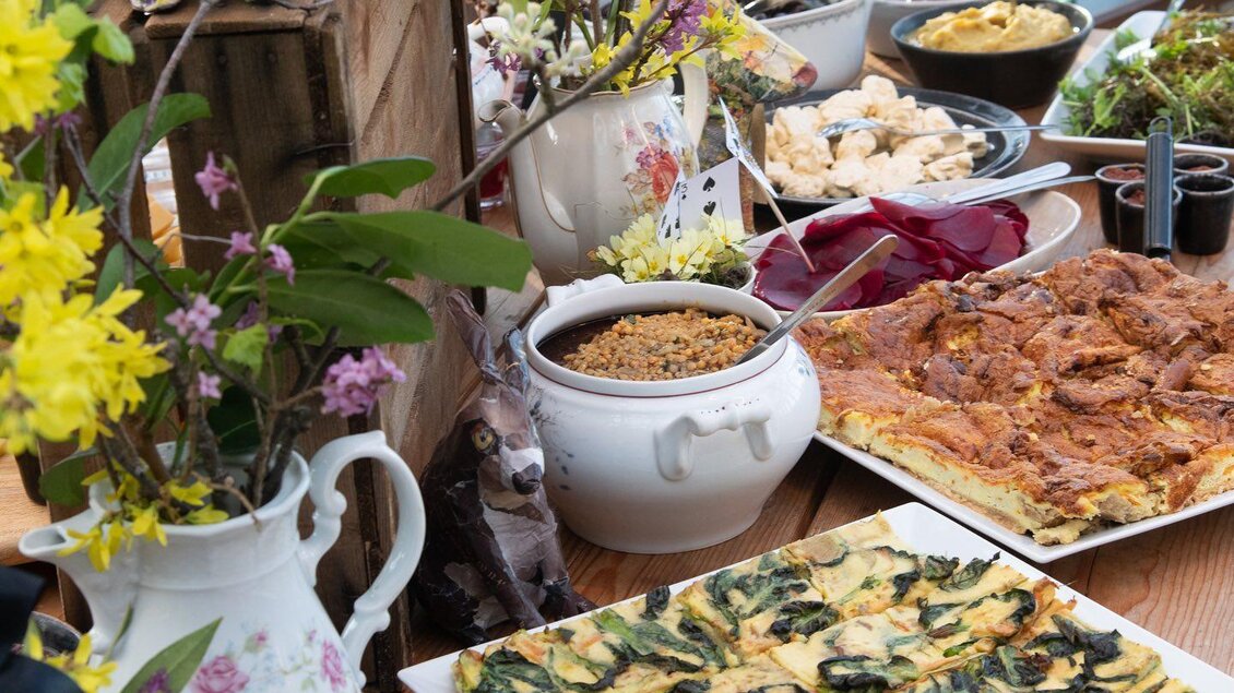 Ein schön dekorierter Tisch mit verschiedenen köstlichen Gerichten und bunten Blumen. Die Speisen sind vielfältig und laden zum Genießen ein. | © Vom Hügel