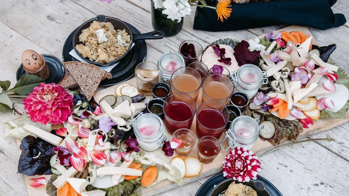 Ein buntes Buffet mit frischem Gemüse, Käse und verschiedenen Getränken. Blumen dekorieren die Anordnung auf einem rustikalen Tisch. | © Vom Hügel