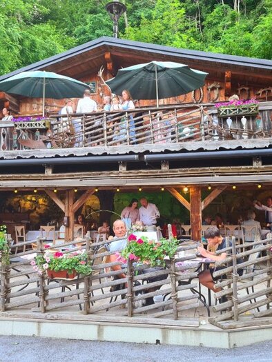 A cozy restaurant with a wooden veranda in the midst of nature. Many guests enjoy the food in nice weather and blooming plants. | © Platzhirsch-Valek