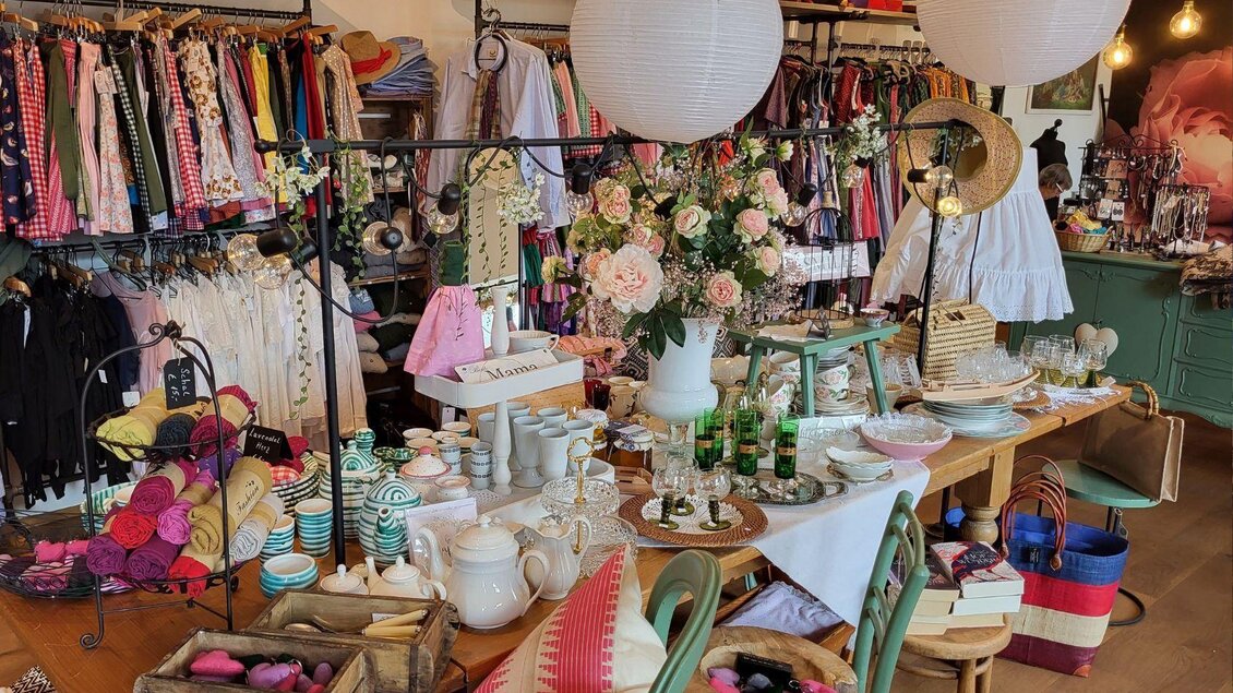 Ein einladendes Geschäft mit bunten Kleidungsstücken und vielen Dekorationsartikeln. Auf einem Tisch sind Geschirr, Blumen und verschiedene Accessoires schön arrangiert. | © Petra Kirchschlager
