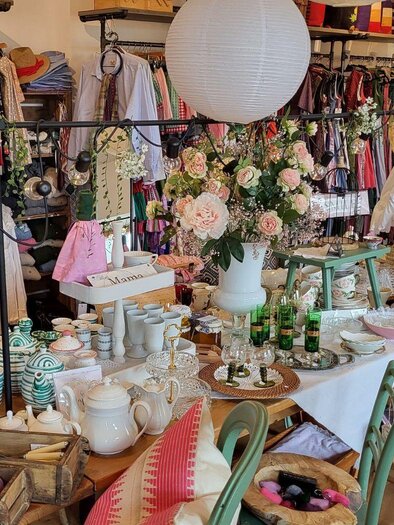 Ein einladendes Geschäft mit bunten Kleidungsstücken und vielen Dekorationsartikeln. Auf einem Tisch sind Geschirr, Blumen und verschiedene Accessoires schön arrangiert. | © Petra Kirchschlager