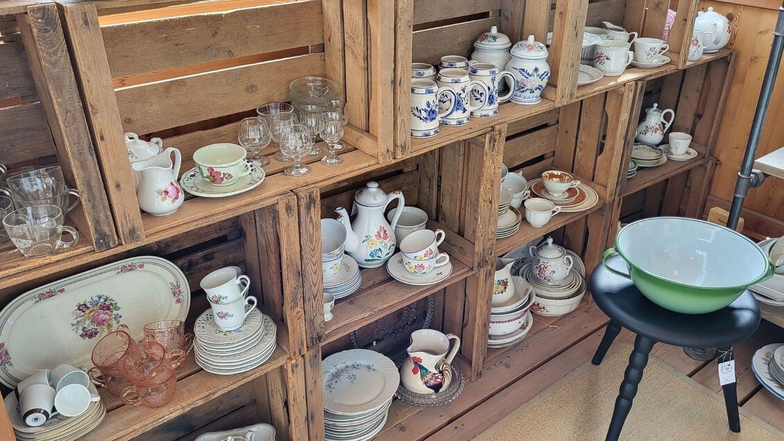 Eine Auswahl an Geschirr und Glaswaren in Holzregalen. Es gibt Tassen, Teller und Teekannen in verschiedenen Designs. | © Petra Kirchschlager