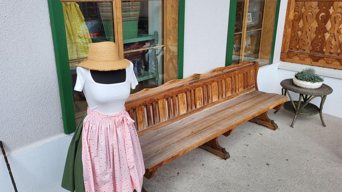 Eine gemütliche Bank vor einem traditionellen Gebäude. Eine Schaufensterpuppe trägt ein typisches Kleid mit einem Röckchen. | © Petra Kirchschlager