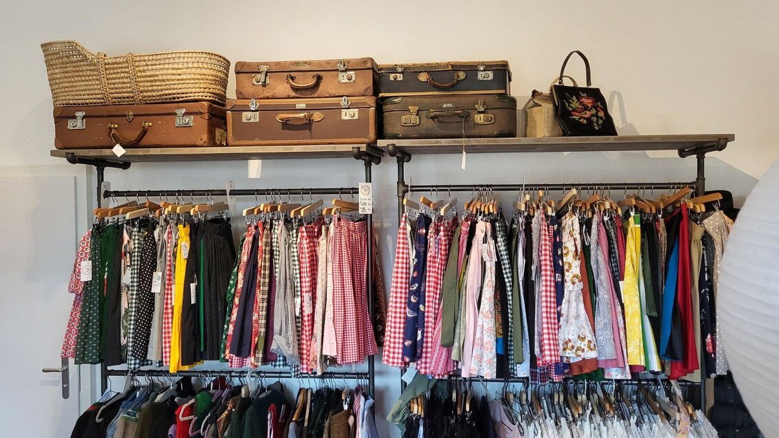 Ein Kleiderregal mit einer bunten Auswahl an Kleidung und Accessoires. Darüber befinden sich mehrere Koffer und eine Tasche. | © Petra Kirchschlager