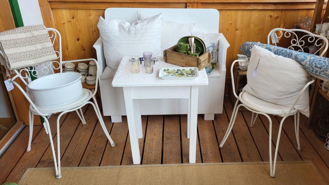 Ein gemütlicher Sitzbereich auf einem Balkon mit einem weißen Tisch und zwei Stühlen. Auf dem Tisch liegen Dekorationsgegenstände und Kissen für zusätzlichen Komfort. | © Petra Kirchschlager