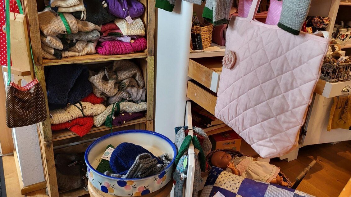 Ein gemütlicher Raum mit Regalen voller handgefertigter Strickwaren. Verschiedene Accessoires und Stoffe liegen verstreut auf dem Boden und in Körben. | © Petra Kirchschlager